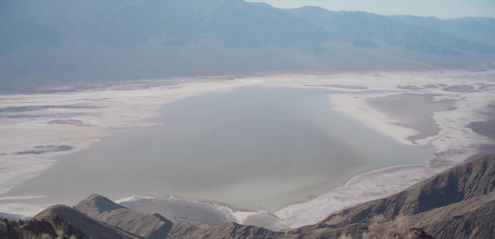 A majestic high-angle tilting shot reveals a vast salt lake nestled within a desert mountain basin