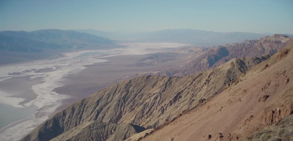 A stunning wide shot from a high vantage point overlooking the vast, arid expanse of a desert valley and salt flats