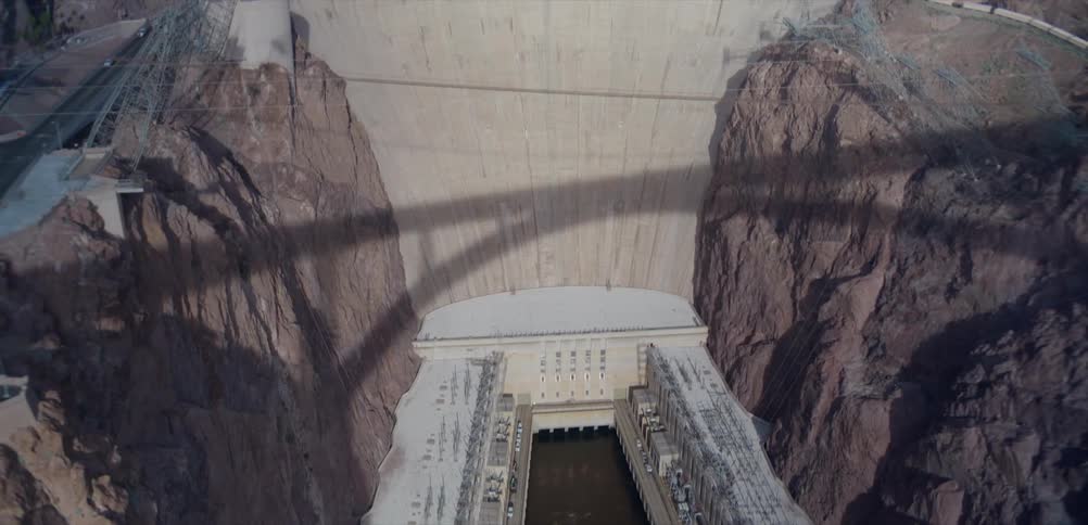An aerial tilt-up shot reveals the massive Hoover Dam, starting from the hydroelectric power plant at the base and ending on the vast Lake Mead reservoir