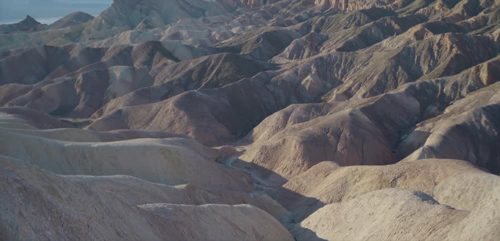 The morning sun casts long shadows over the expansive, multi-colored badlands and mountains of Zabriskie Point