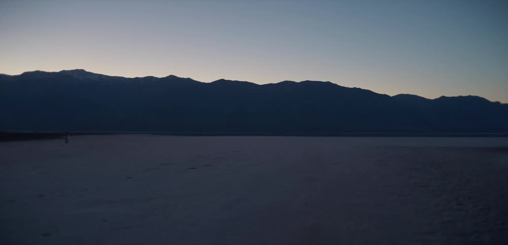 The expansive salt flats of Death Valley stretch out towards a silhouetted mountain range during a serene twilight