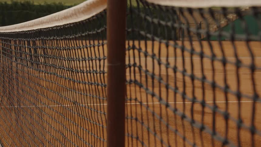 A detailed close-up shot of a tennis net on an empty red clay court