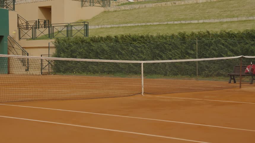 A yellow tennis ball is hit back and forth over the net in slow motion on an empty clay court