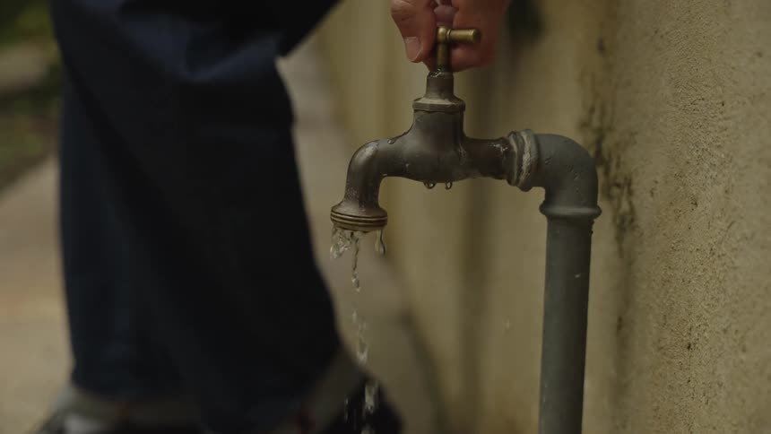 A slow motion close up of a person's hand turning off an old outdoor water spigot