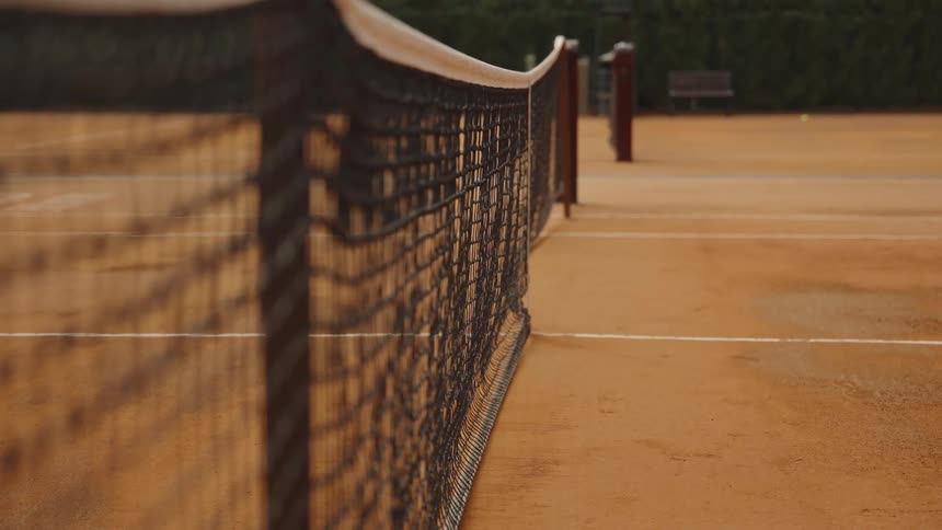 A tennis ball bounces in the background of a close-up shot of the net on a clay tennis court