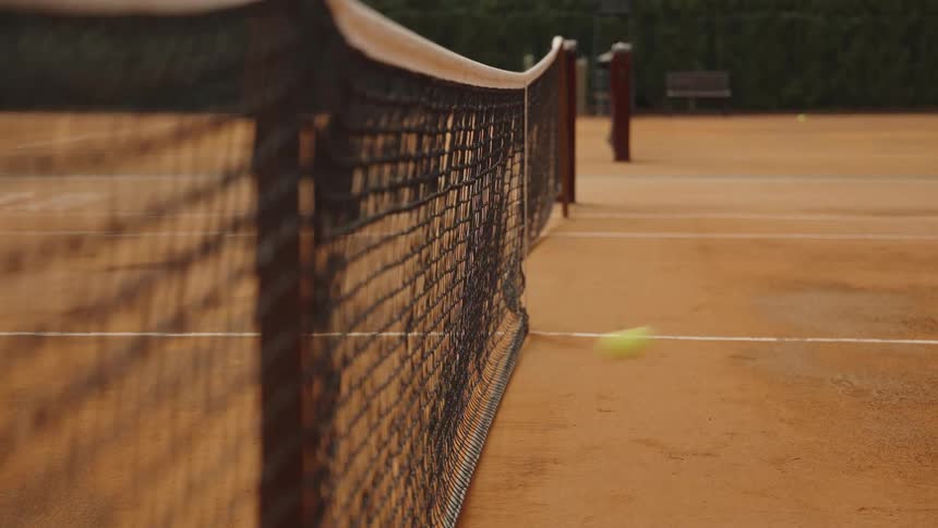 A tennis ball flies into the net and bounces on the clay court in a dramatic slow-motion close-up shot