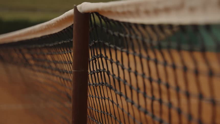 A detailed rack focus shot of a tennis net on an empty clay court