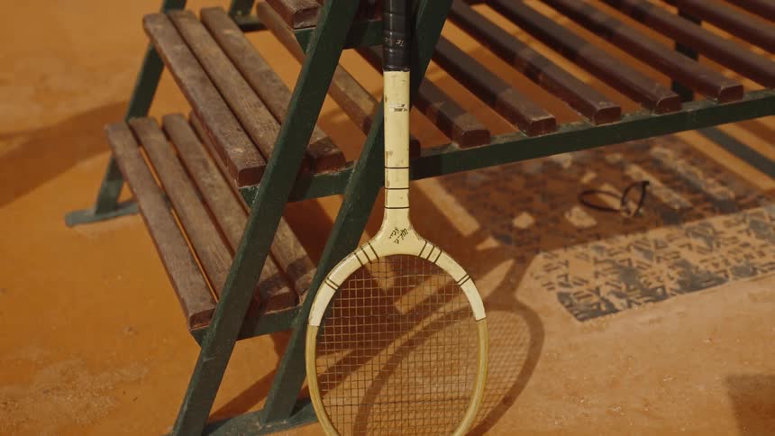 A vintage wooden tennis racket leans against a rustic umpire's chair on a classic clay court
