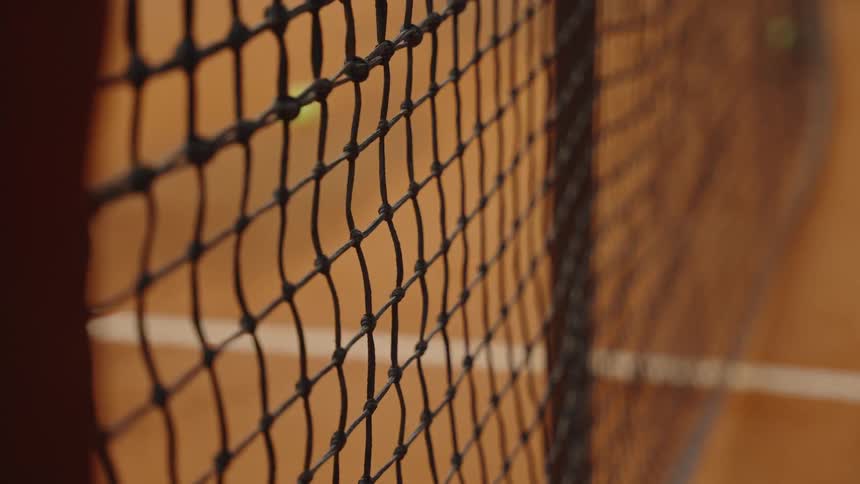 Dramatic slow motion close-up of a tennis ball flying over the net and landing on a clay court