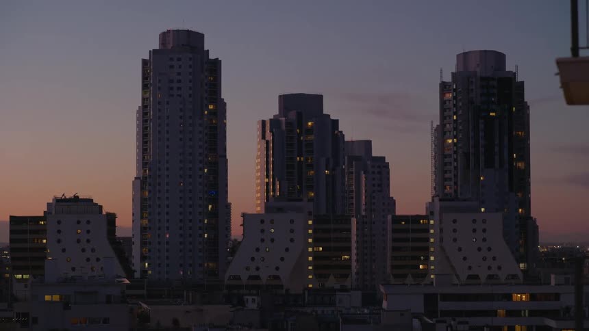 A serene view of modern city skyscrapers as lights begin to twinkle against the colorful dusk sky