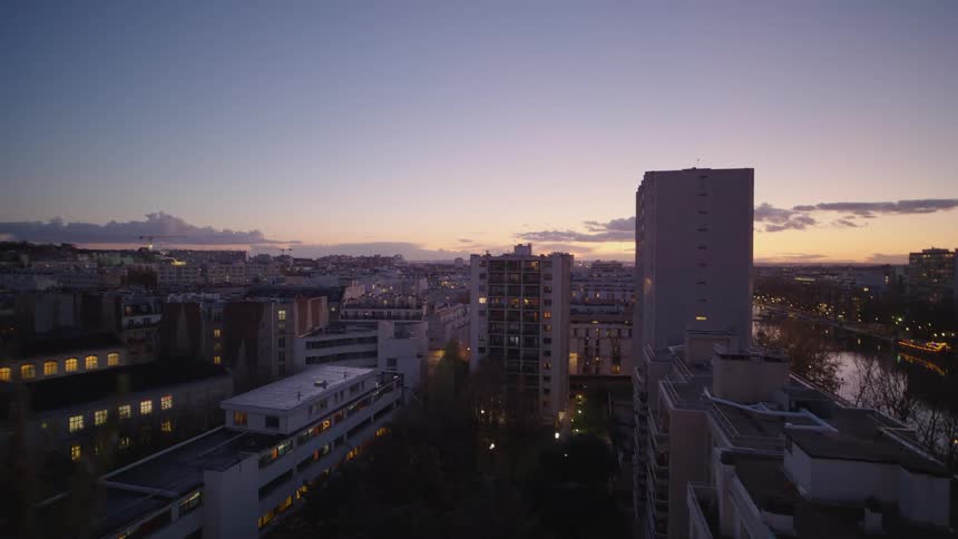 A static wide shot of a city skyline at dusk, capturing the transition to night as lights illuminate apartment buildings