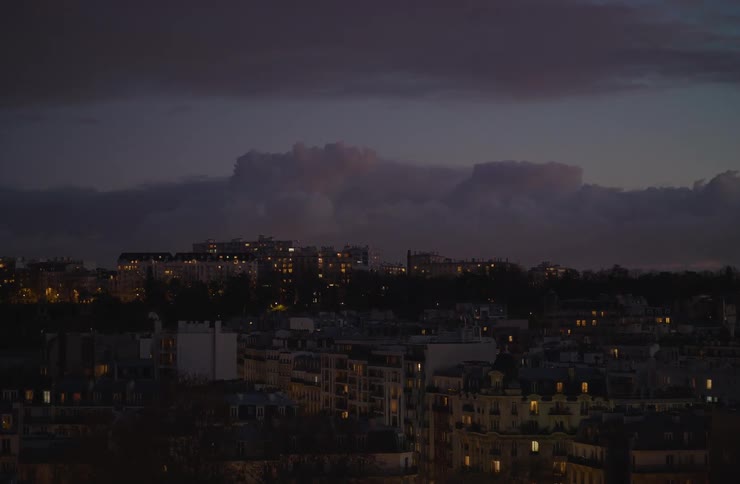A wide view of the Paris skyline shows city lights twinkling at dusk under a dramatic, moody purple sky
