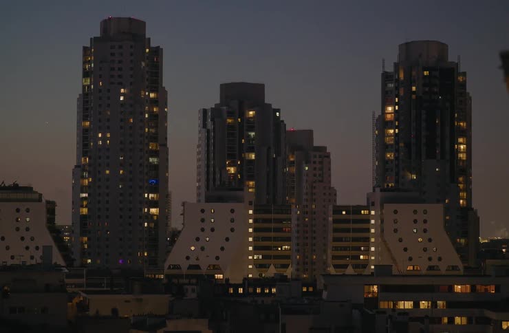 The glowing windows of a distinctive modern apartment complex illuminate the cityscape against a dark twilight sky