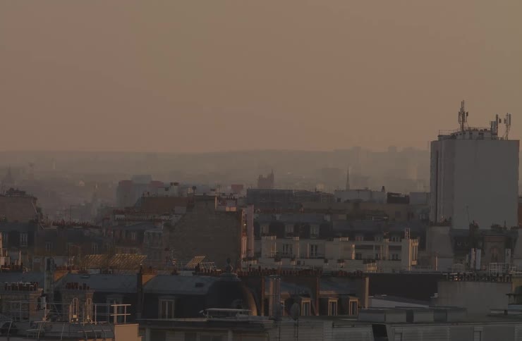 A hazy view of Parisian rooftops basks in the warm glow of a golden hour sunset