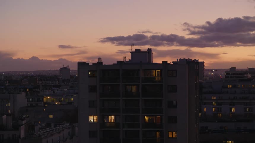 A large city apartment building is silhouetted against a beautiful sunset sky as lights turn on in the windows