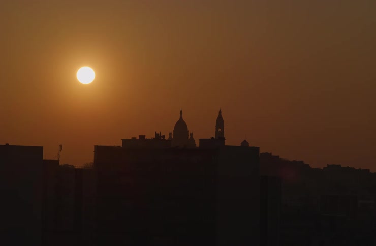 The sun shines brightly over the silhouetted skyline of Paris, France, highlighting the famous Sacré-Cœur Basilica at sunset