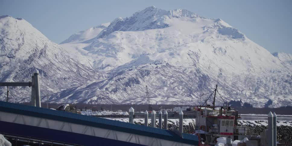 Majestic snow-capped mountains provide a stunning backdrop for a snowy fishing harbor on a clear winter day