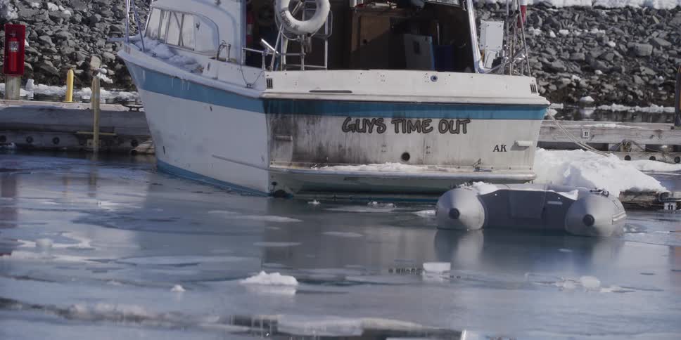 An Alaskan boat named 'Guy's Time Out' sits docked in a cold, icy harbor during a winter freeze