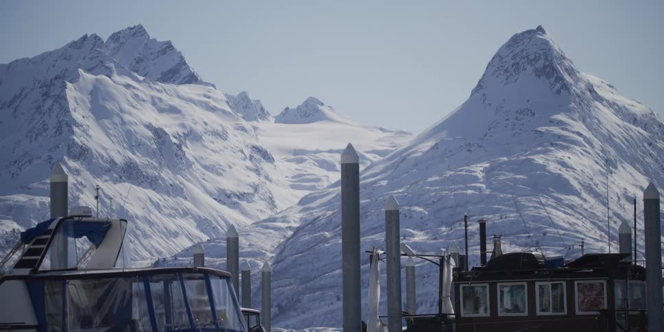 Majestic snow-covered mountains and a glacier tower over boats docked in a serene Alaskan harbor