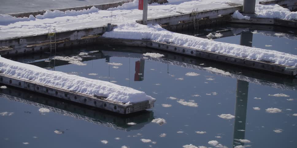 Empty snow-covered docks at a marina with ice floating in the cold water