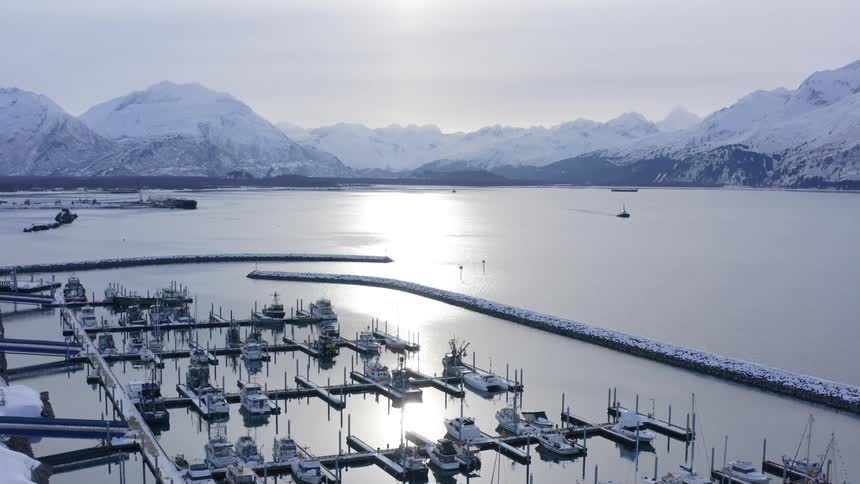 A serene aerial shot slowly pushes in on a tranquil, snow-covered boat harbor nestled among majestic mountains during winter