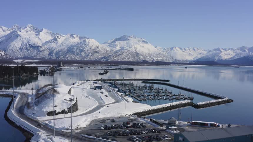 A stunning aerial view of a snow-covered harbor nestled at the base of majestic mountains on a clear winter day