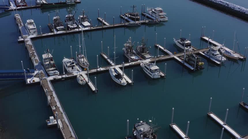 Slow aerial push-in of a tranquil, snow-covered boat harbor in winter with various vessels docked