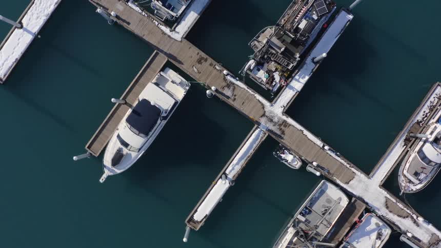 Aerial top-down view of snow-covered boats docked at a marina during a sunny winter day
