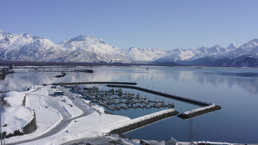 An expansive aerial view of a snowy boat harbor nestled among majestic snow-capped mountains on a clear winter day