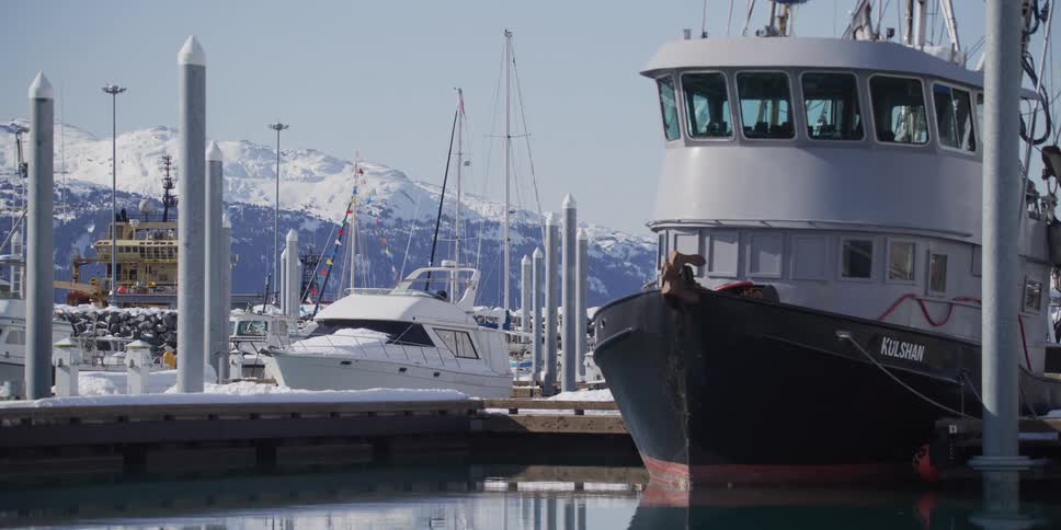 A peaceful winter scene of boats docked in a snowy harbor with majestic snow-capped mountains in the background