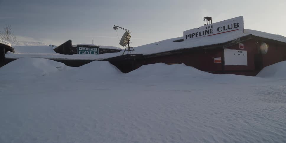 The exterior of The Pipeline Club is buried in deep snow drifts during a cold winter day