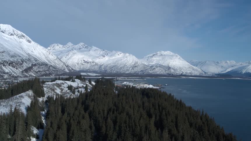 A stunning aerial view of a snow-covered town and harbor nestled between a dense forest and majestic mountains in a winter landscape