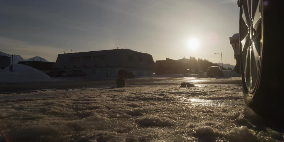 A small rabbit hops and forages for food on an icy, snow-covered street in a small town as the sun sets in the background