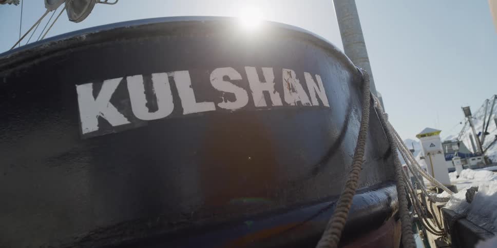 Low angle shot of the name 'Kulshan' on a docked boat in a snowy harbor on a bright, sunny day