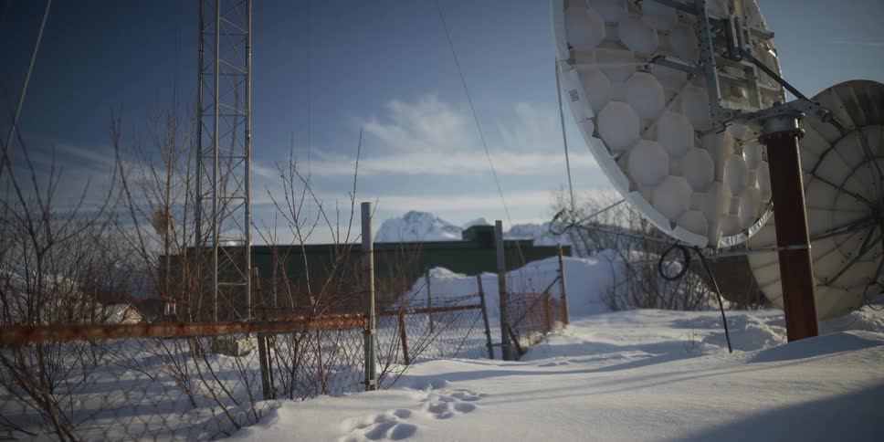 Slow dolly shot reveals a large satellite dish at a remote snowy station with mountains in the background