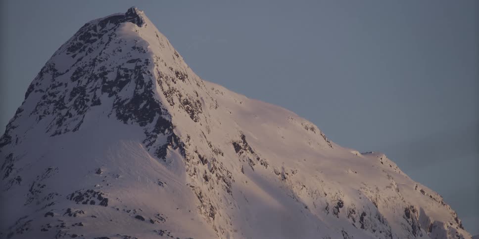 The majestic peak of a snow-covered mountain is bathed in the warm, golden light of dawn