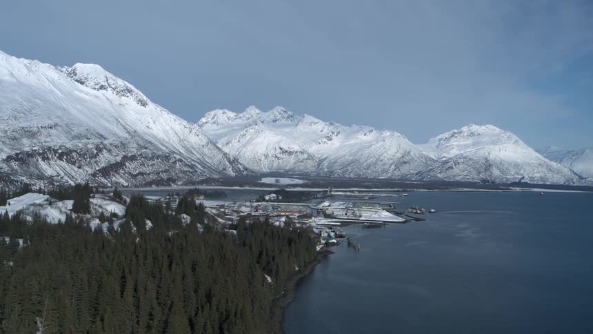 Expansive aerial view of the port of Valdez, Alaska, surrounded by the snow-capped Chugach Mountains in winter