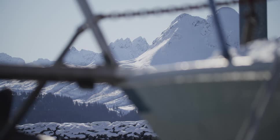 A majestic snow-covered mountain range is framed by the out-of-focus bow of a boat in a snowy landscape on a sunny day