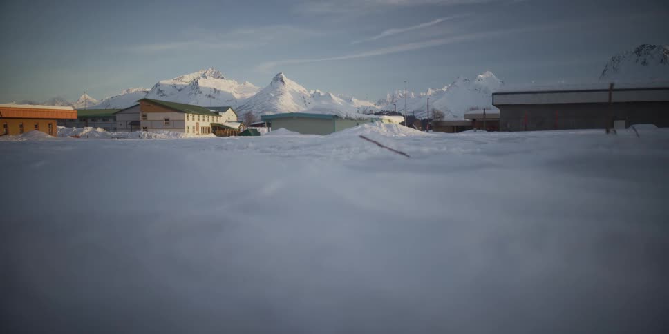 A slow pan reveals a tranquil, snow-covered village nestled at the base of a majestic mountain range in winter
