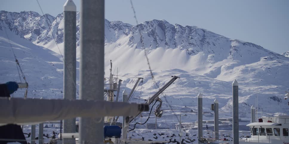 A scenic view of a majestic snow-covered mountain range from a quiet harbor on a sunny winter day