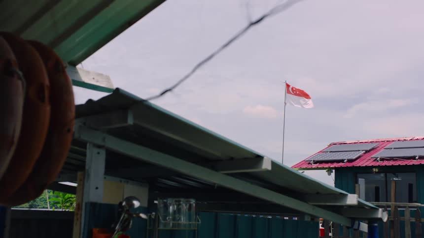 A Singaporean flag waves in the wind above a building with solar panels on a cloudy day