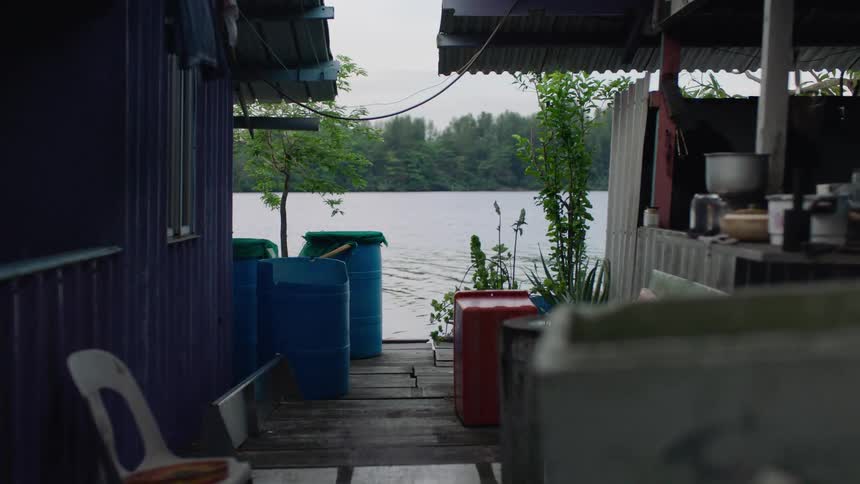 A dog runs along the wooden deck of a floating house as a motorboat glides by on the calm water