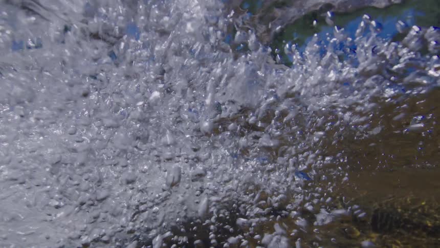 An immersive slow-motion view from underwater captures the chaotic beauty of bubbling rapids in a clear stream
