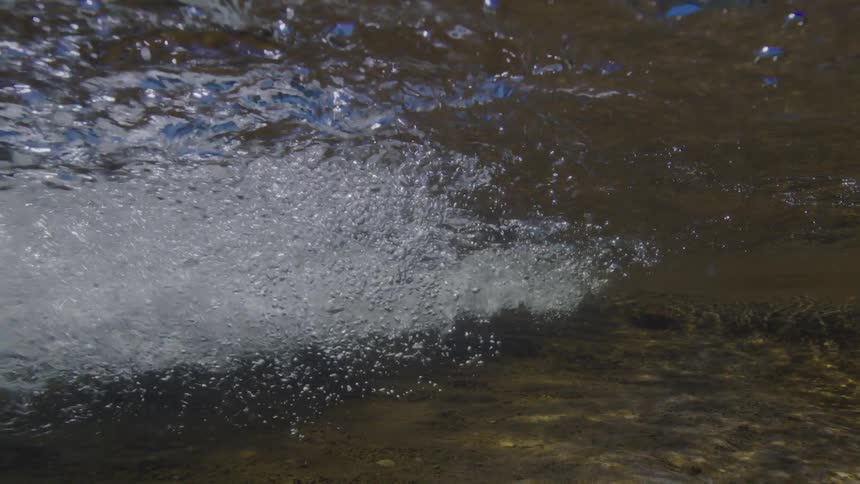 An underwater view captures a powerful stream of bubbles flowing through a shallow river in slow motion