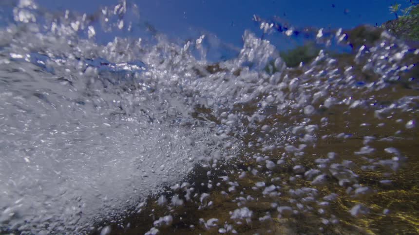 An immersive, slow-motion, underwater perspective captures turbulent bubbles churning in a stream against a brilliant blue sky