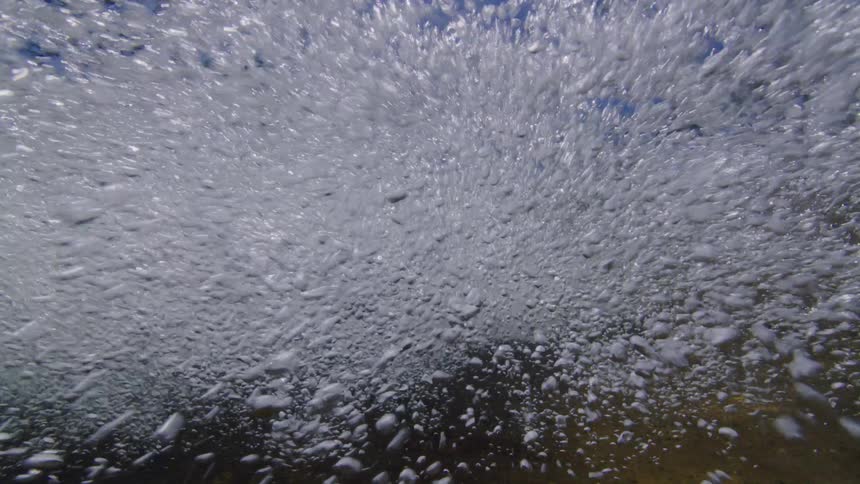 A powerful underwater view from below shows a constant stream of churning bubbles rising to the surface