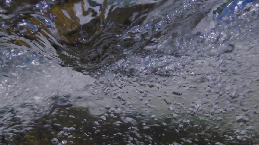 An immersive underwater view captures the turbulent surface and bubbling current of a river in slow motion