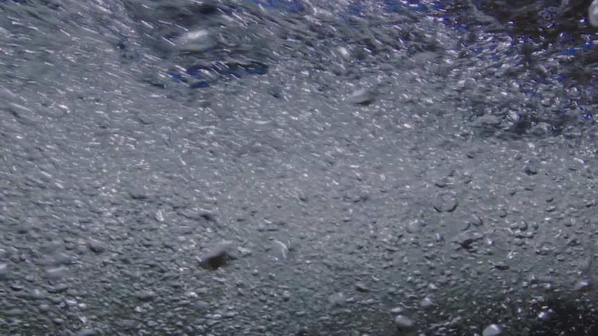 An abstract underwater view of thousands of tiny bubbles rushing through turbulent water