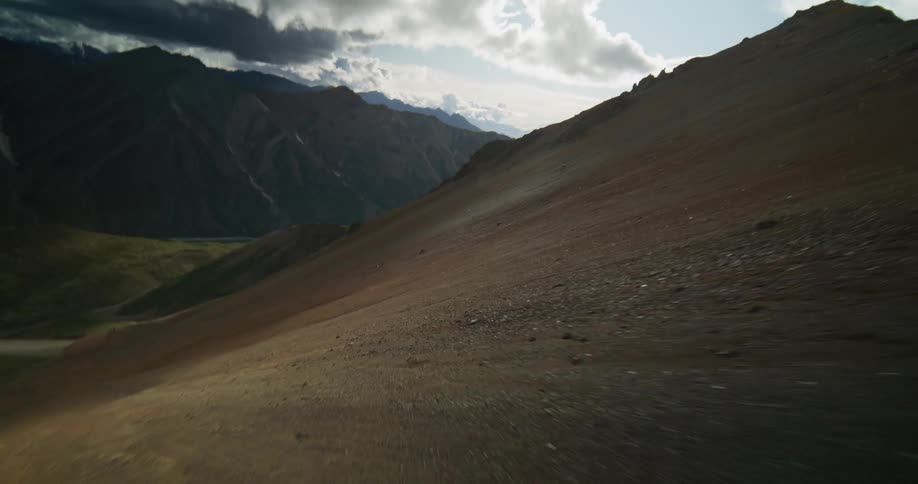 A soaring aerial flyover reveals a vast and rugged mountain valley on a partly cloudy day