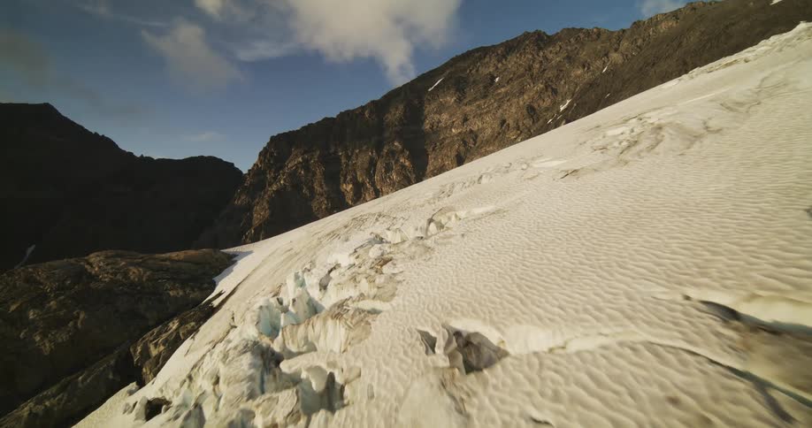 A breathtaking aerial shot flies over a massive, crevasse-filled glacier nestled between rugged mountains at golden hour